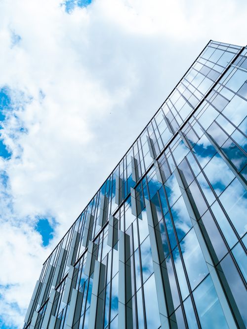 Free Modern glass building reflecting the blue sky and clouds, captured in a low angle view. Stock Photo