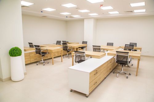 Free A bright, modern office space featuring wooden desks, rolling chairs, and ample lighting. Stock Photo