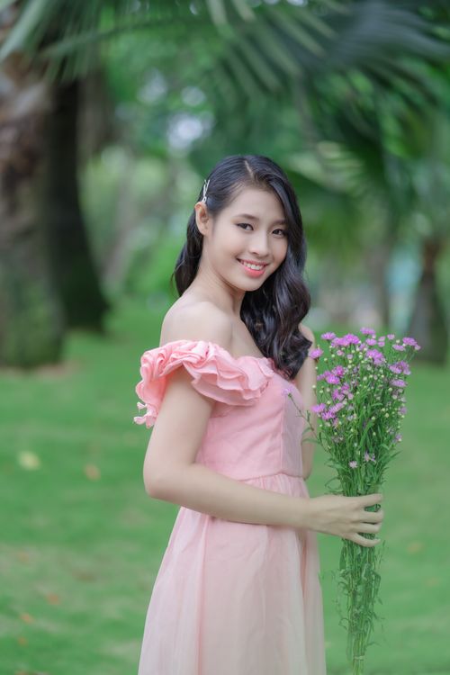 Free Beautiful woman in pink dress with long black hair holding purple flowers in a lush green park. Stock Photo