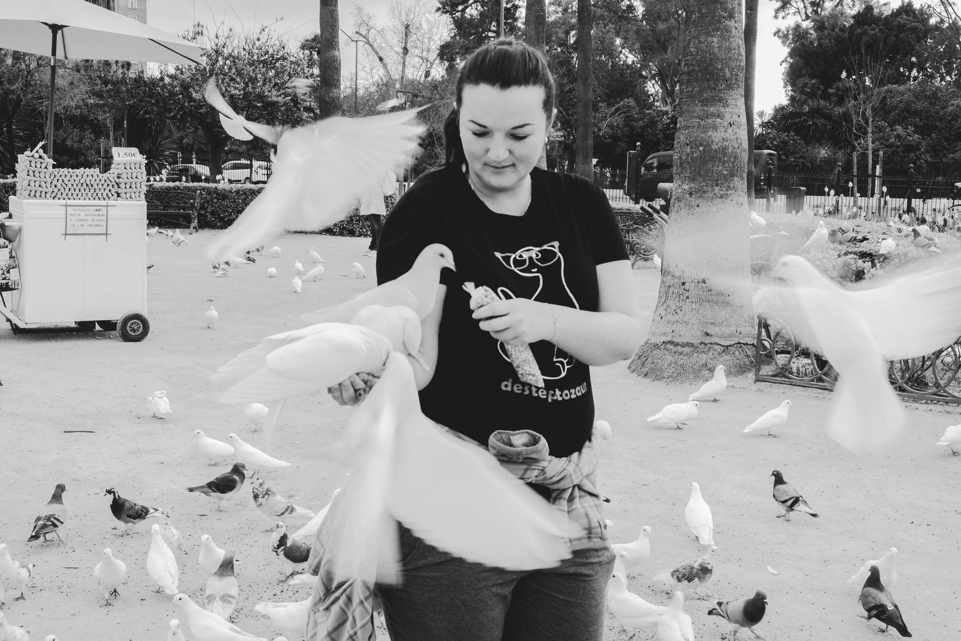 A woman surrounded by white doves and pigeons in a park, captured in black and white.