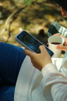 Relaxing moment as a woman enjoys her coffee while browsing on her smartphone.