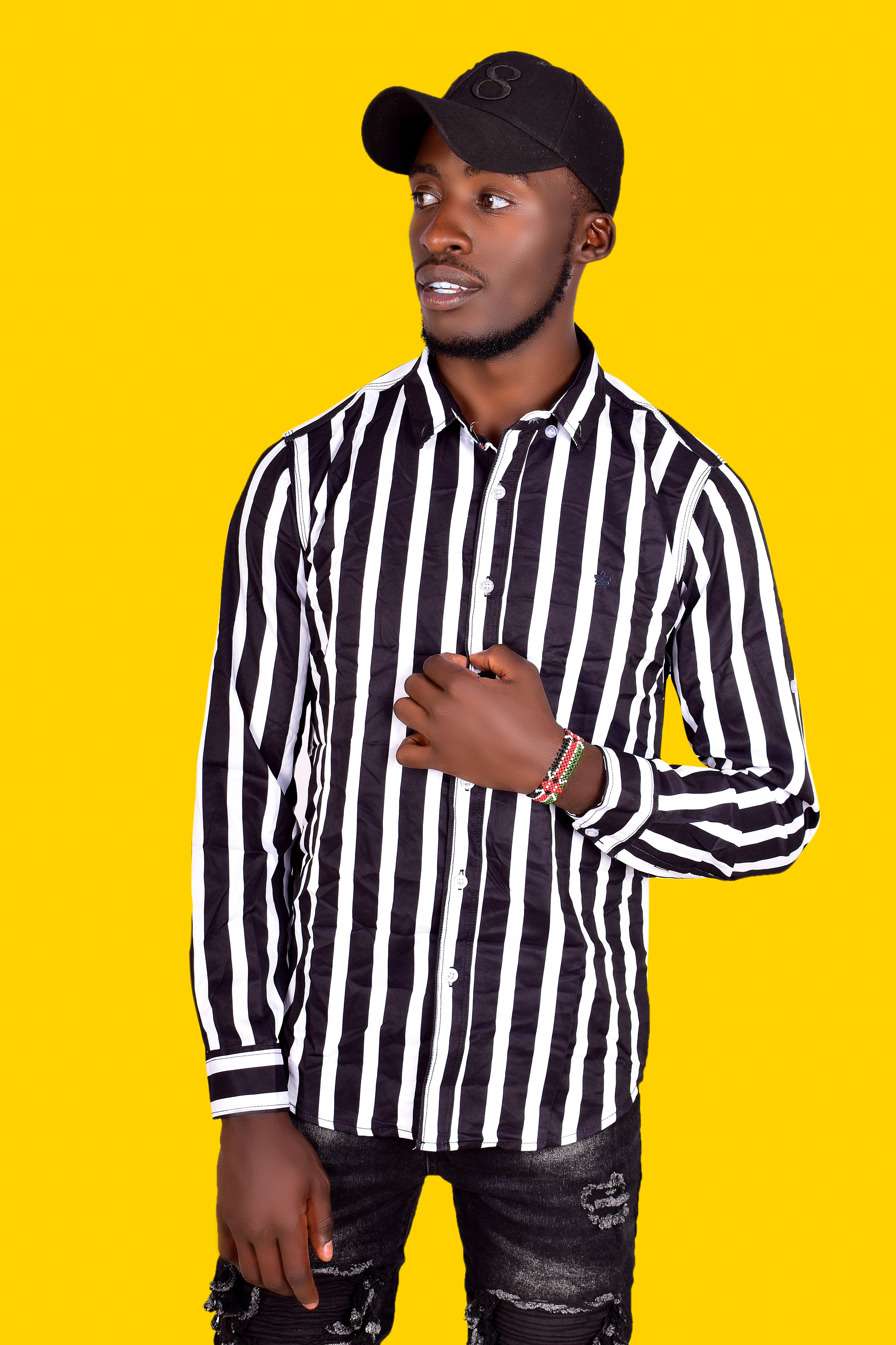 Fashionable African American man wearing a striped shirt against a yellow background, exuding confidence.
