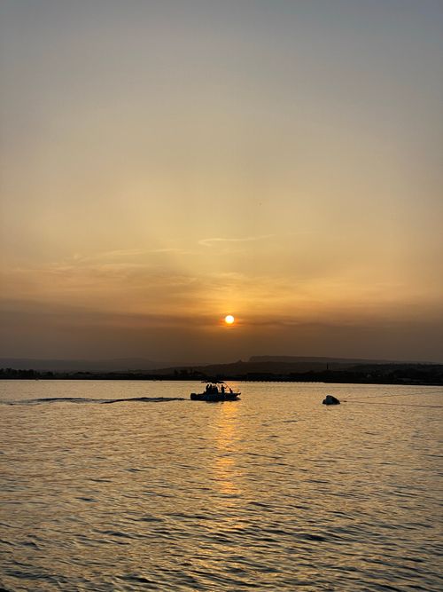 Free A tranquil scene of a boat sailing at sunset in Sicily with calm waters, perfect for travel and nature themes. Stock Photo