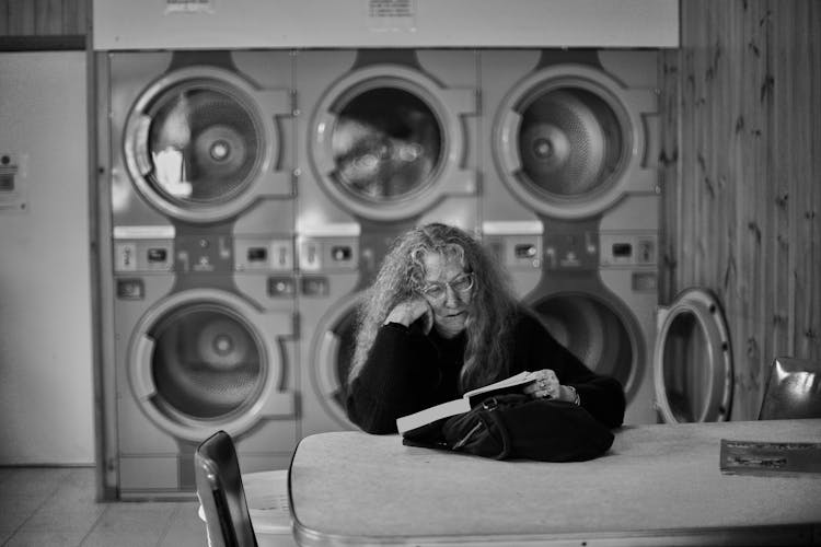 Elderly Woman Reading A Book In A Laundry Facility 