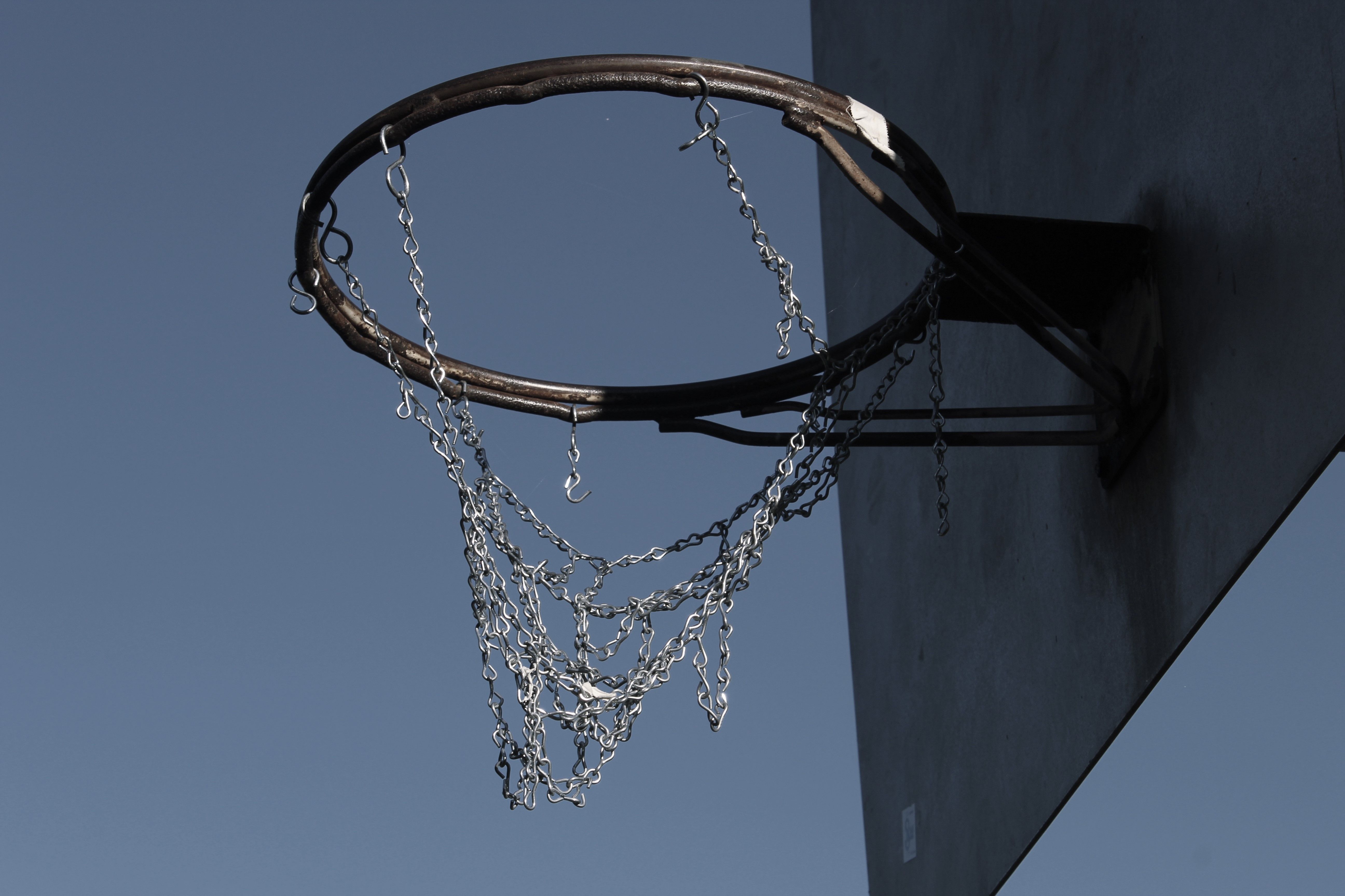 A weathered basketball hoop with a chain net against a clear blue sky, captured in Newark, DE.
