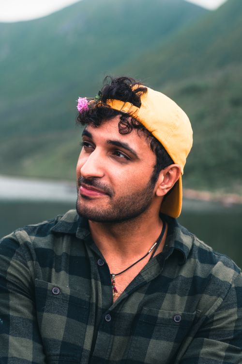 Free A contemplative man with a yellow cap and flower, set against a lush outdoor backdrop. Stock Photo