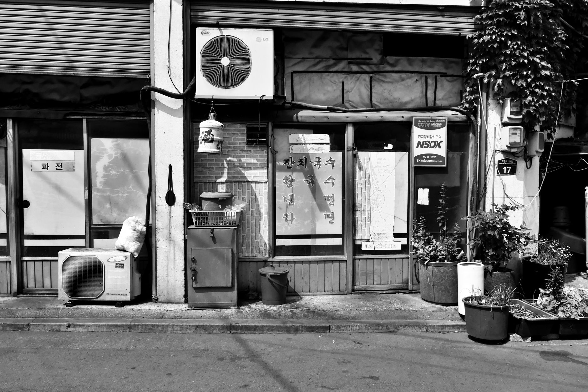 A black and white photo of a small storefront with vines and signs, showcasing urban charm.