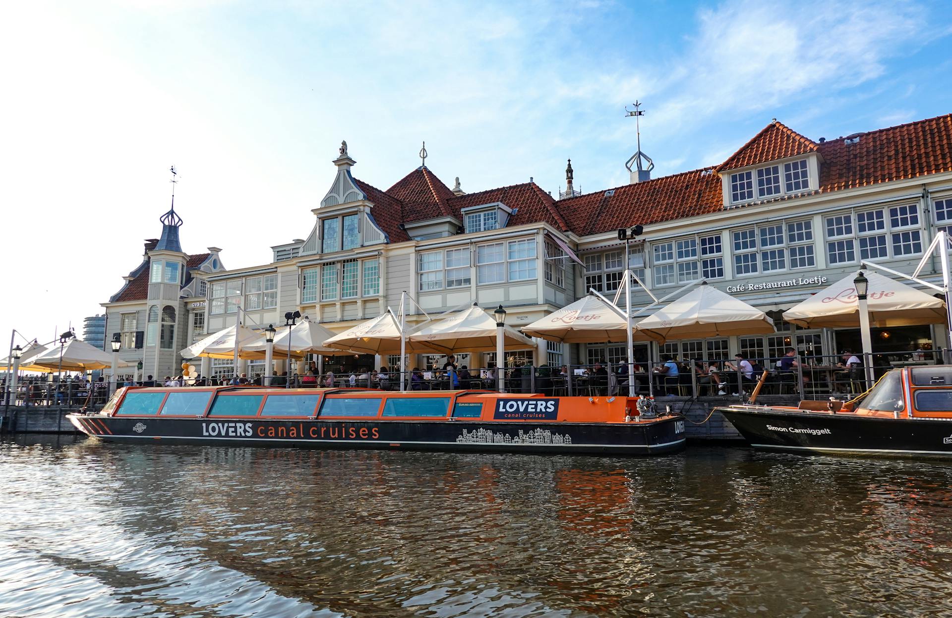 Scenic view of Amsterdam canal with historic Dutch buildings and canal cruise boats under a clear sky.