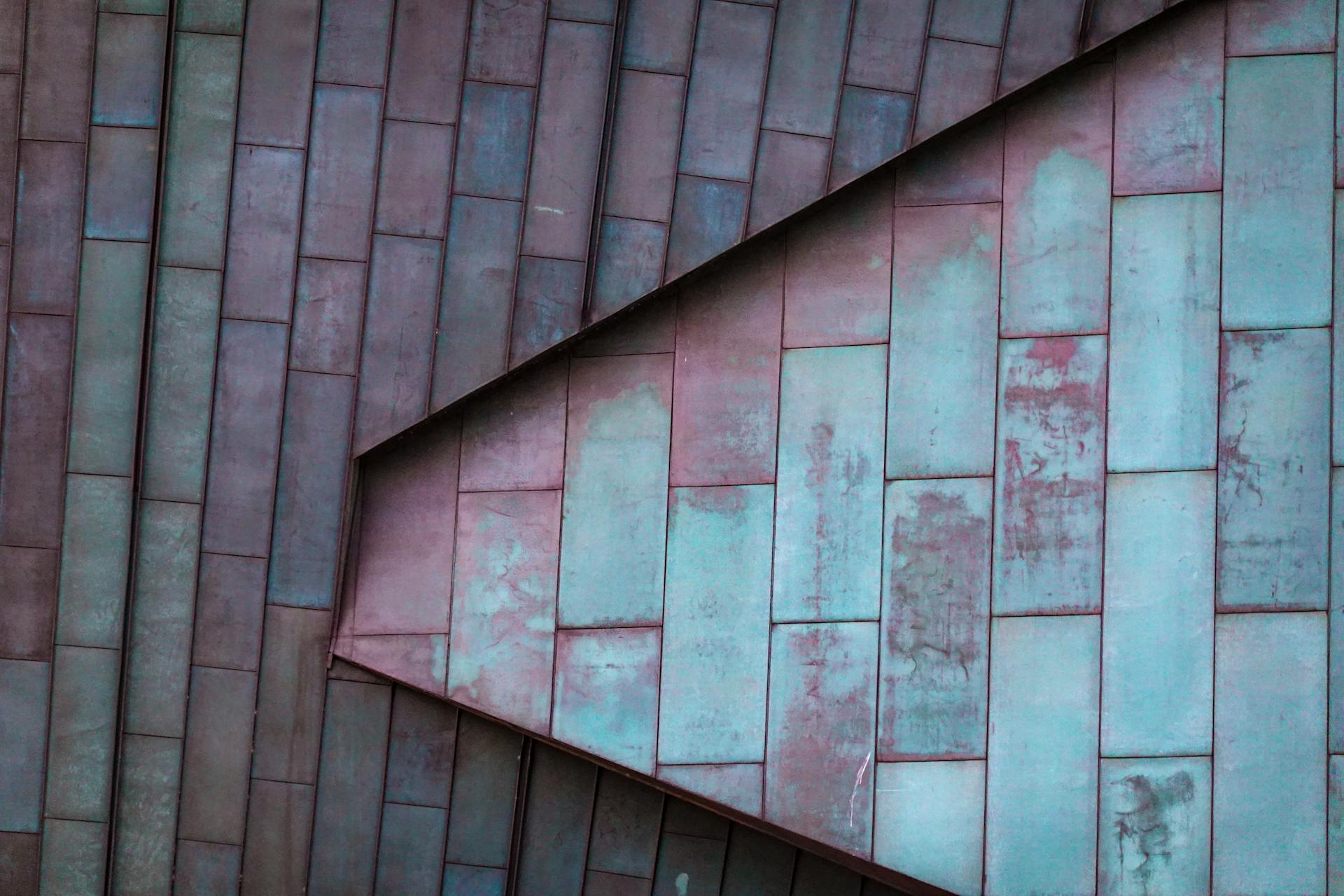 Close-up view of weathered metal roof tiles with faded and patina effect, capturing geometric patterns and textures.