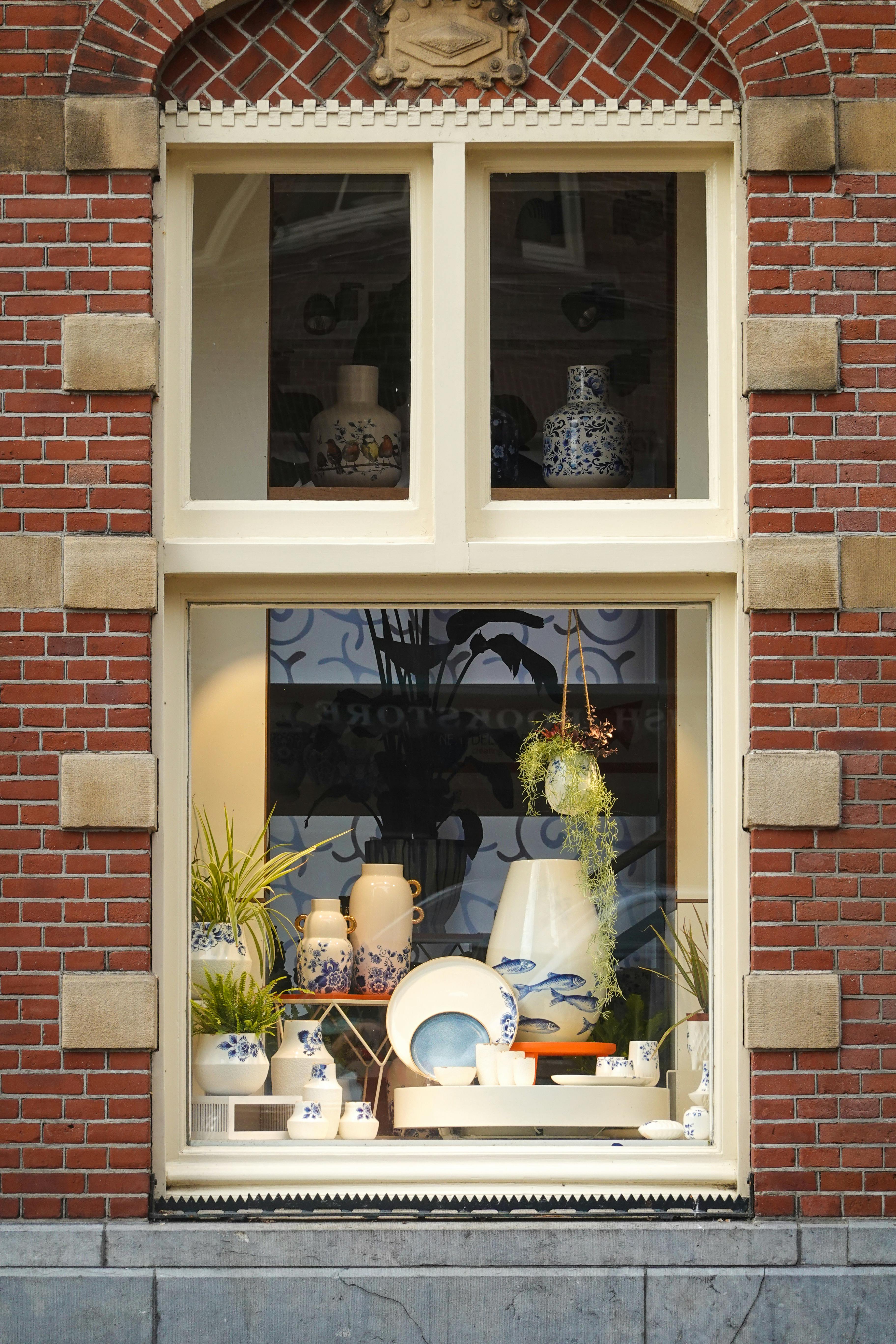 Beautiful window display of blue and white ceramics in a classic brick building facade.