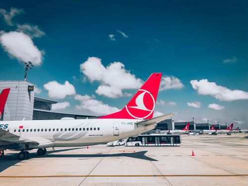 Free Airplanes on a tarmac at an airport with red tail logos, clear blue sky, and scattered clouds. Stock Photo
