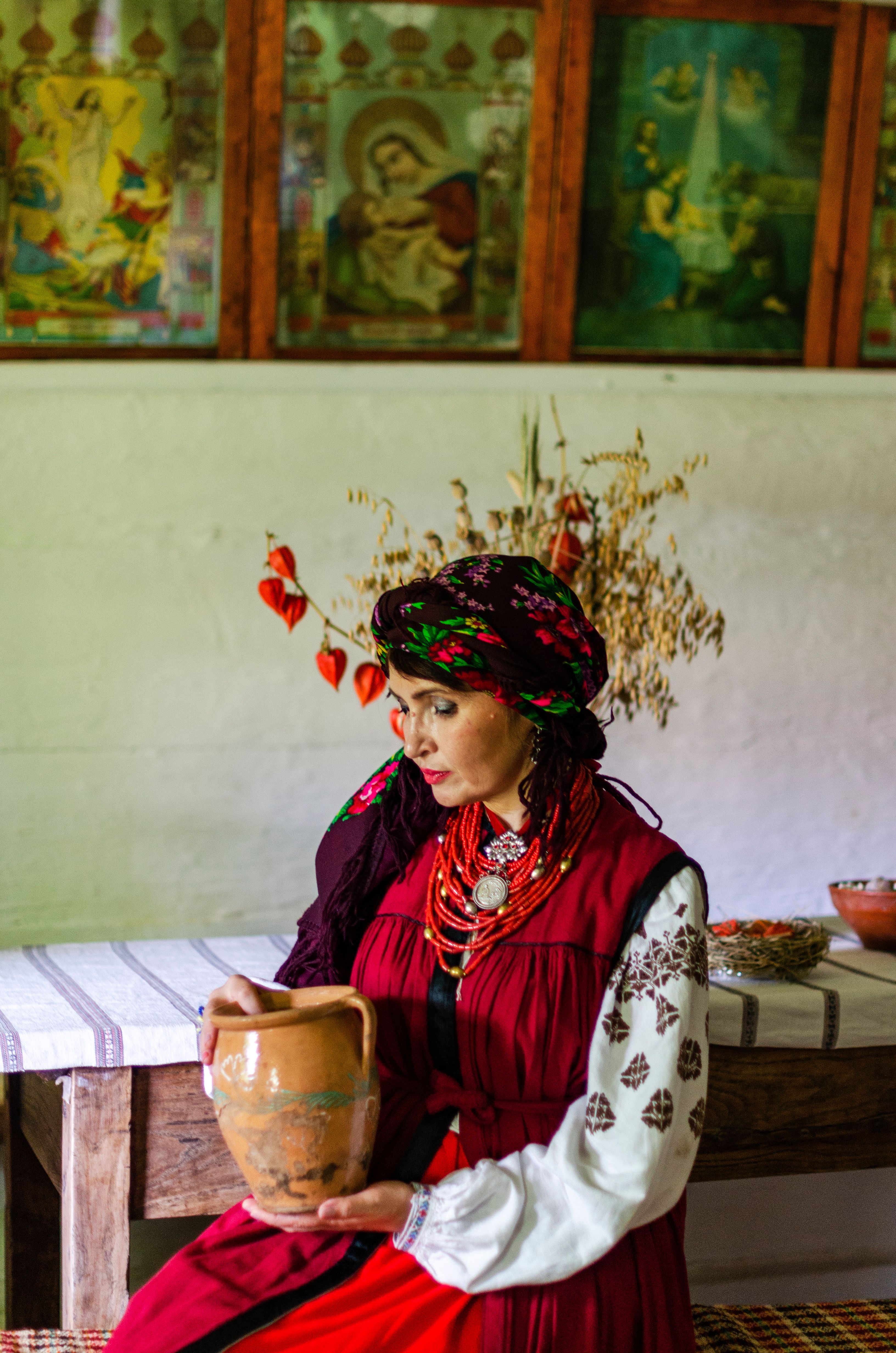 Beautiful Ukrainian woman in traditional attire holding a clay jar indoors.