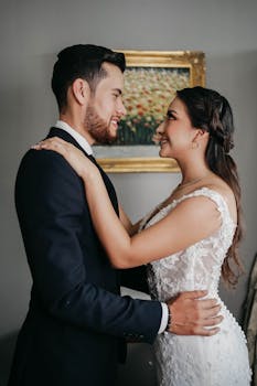 A loving couple shares a romantic embrace on their wedding day, indoors.