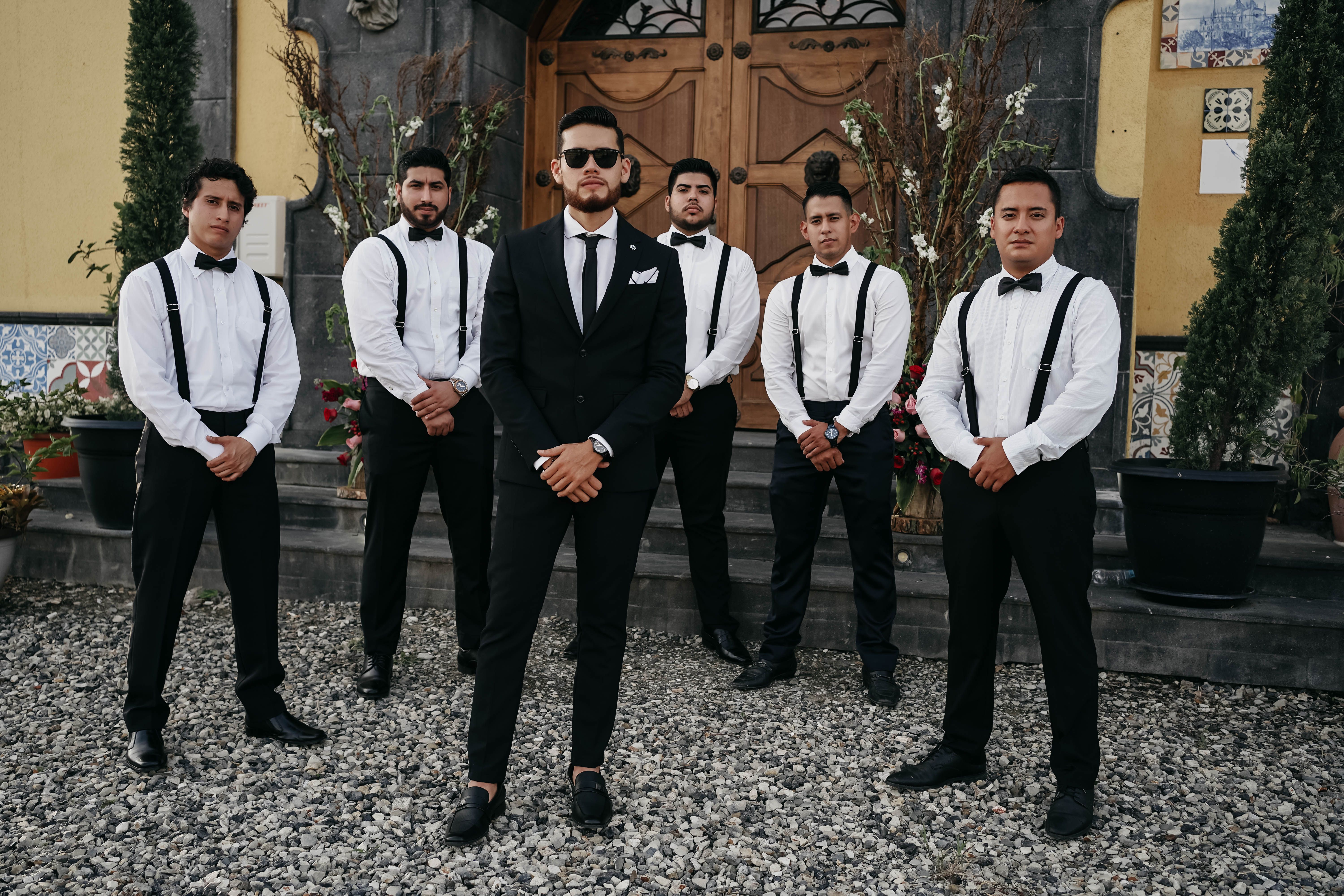 groomsmen group portrait outdoors in matching charcoal suits with boutonnieres, sunlit garden venue grounds, relaxed natural pose