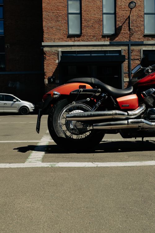 Free A red motorcycle parked in an urban setting with a brick building backdrop. Stock Photo