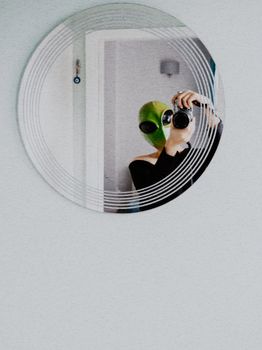A person wearing an alien mask takes a selfie in a round mirror, capturing a playful Halloween theme.