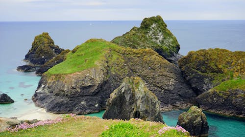 Rock Formation Coated With Green Grass on Body of Water