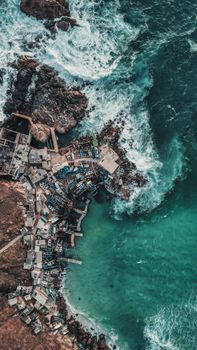 Stunning aerial photograph of a coastal city with rocky shore and vibrant ocean waves.