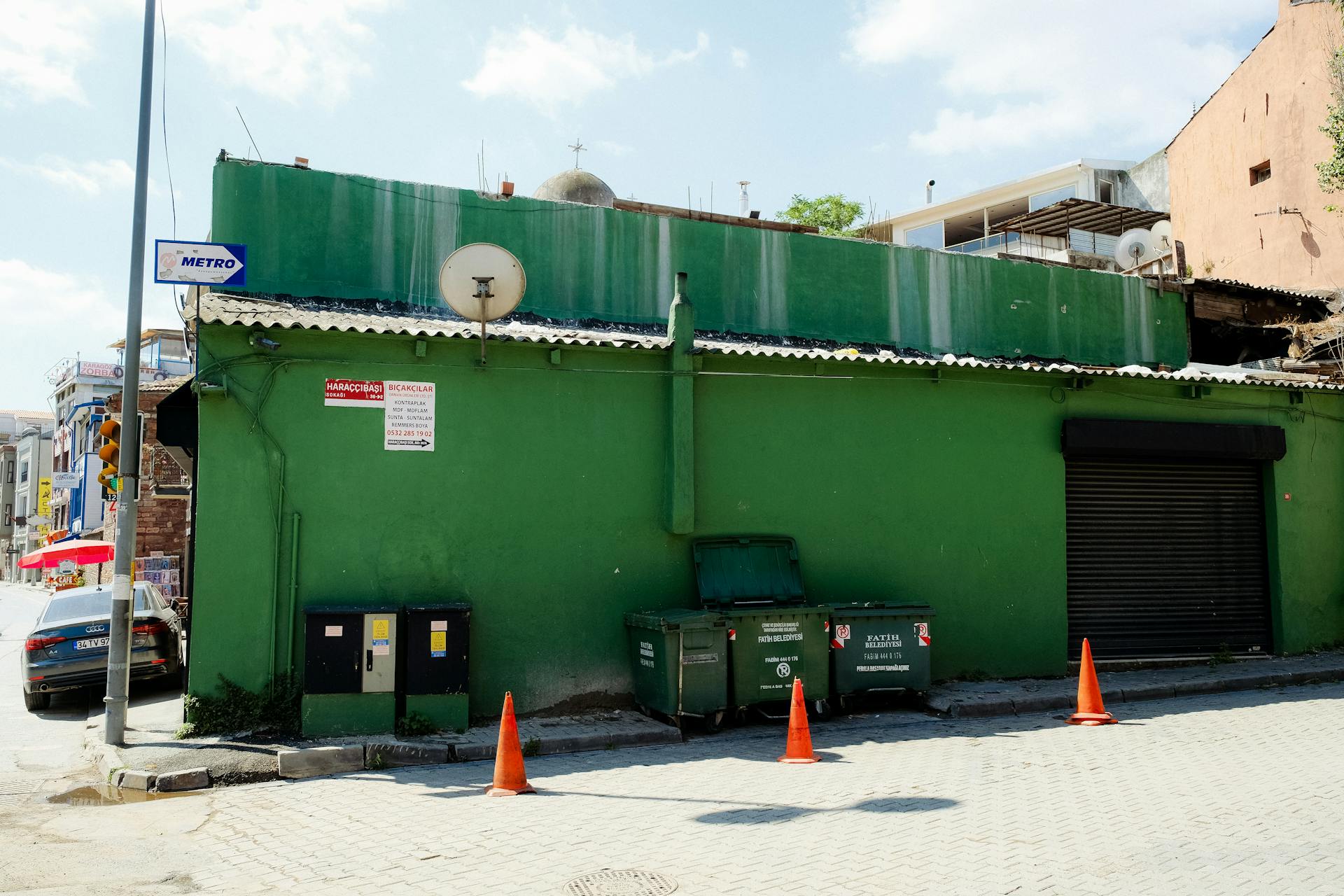 Street view of a vibrant green building with a dumpster on a sunny day.