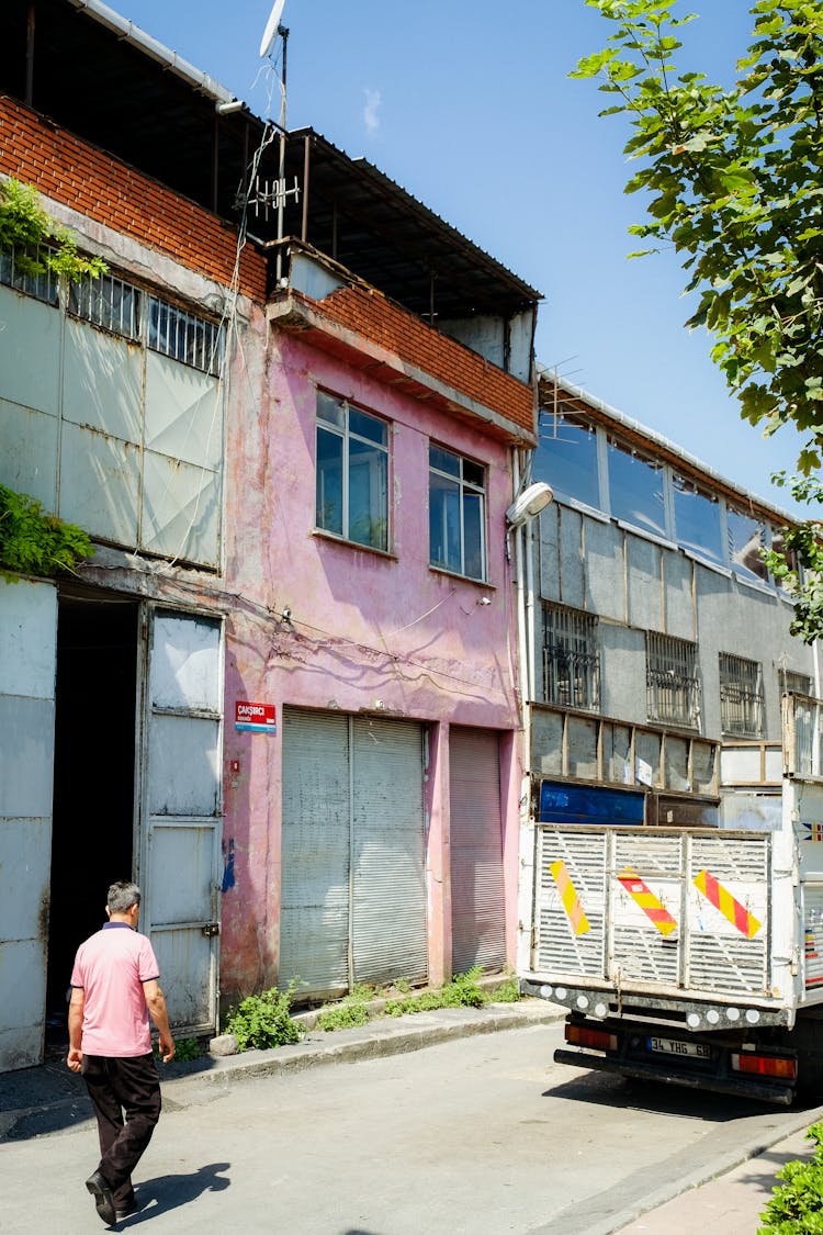 Man Wearing A Pink T-Shirt Walking In An Industrial Area Behind A Truck