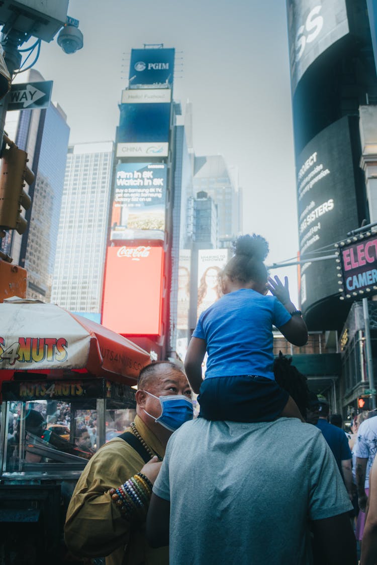 Photo Of A Man In A Face Mask Talking To A Man With A Child On His Shoulders In Times Square, New York, USA