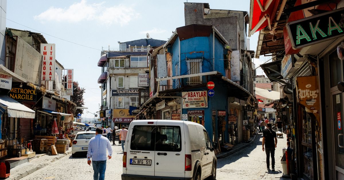 A vibrant narrow street in Istanbul with shops, people walking, and moving vehicles.