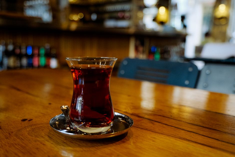 A close-up of traditional Turkish tea served in a tulip glass on a wooden table in a cozy cafe.