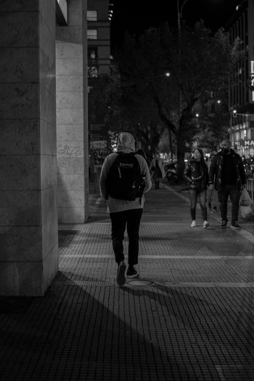 Grayscale Photo of People Walking on the Sidewalk during Nighttime