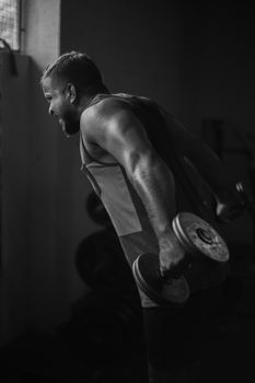 A muscular man lifting dumbbells in a dramatic black and white gym setting.
