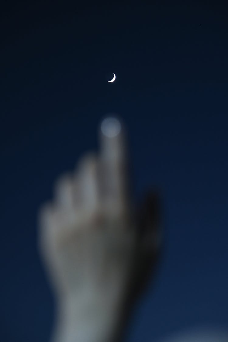 Photo Of A Blurred Hand And Finger Point To The Moon At Night