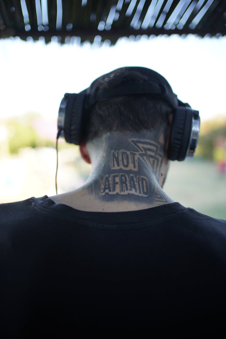 Back View Of A Tattooed Man In Black Shirt Wearing Headphones