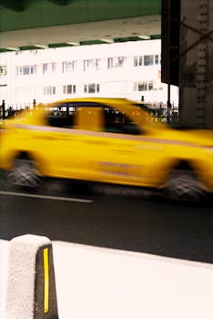 Blurred motion of a yellow taxi speeding through a city street under a bridge, capturing urban nightlife.