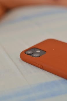 Minimalist image of a smartphone with a distinctive orange case on a soft surface.