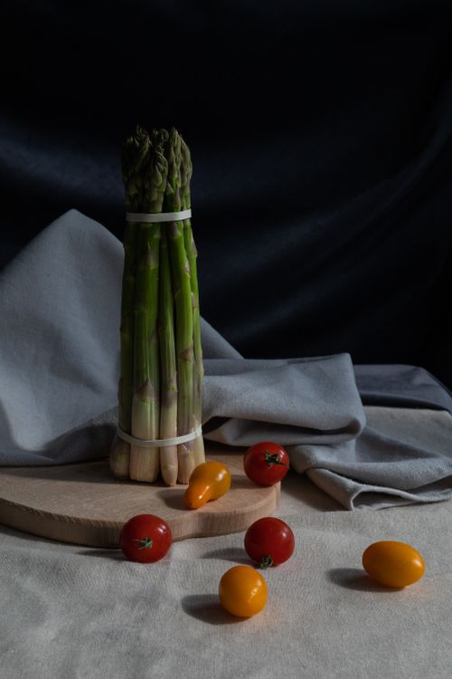 Free A bundle of fresh asparagus with colorful cherry tomatoes on a wooden board, styled with a cloth. Stock Photo