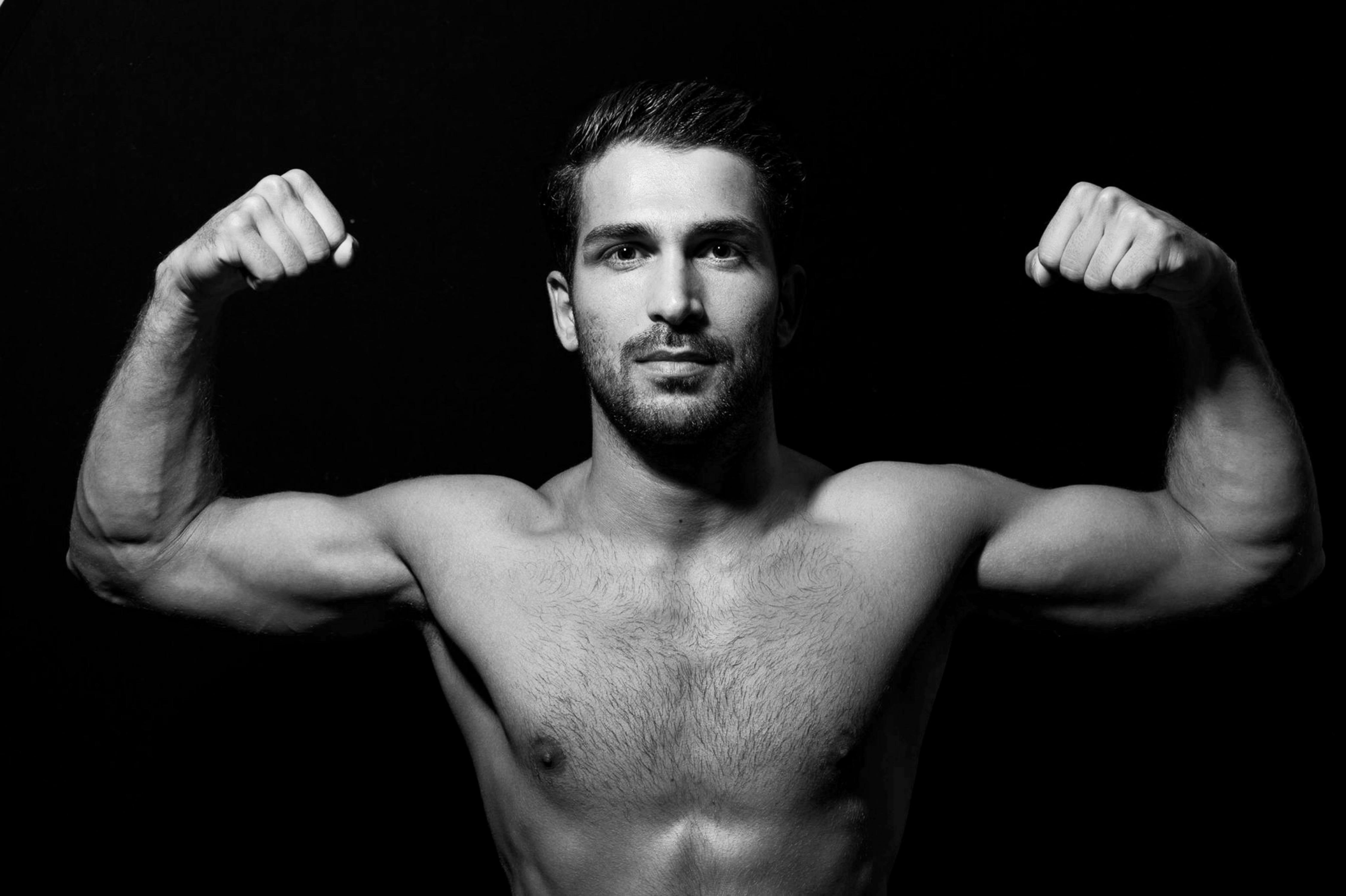Monochrome close-up of a muscular man flexing, showcasing strength and fitness in a dramatic pose.
