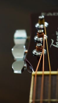 Macro shot of an acoustic guitar headstock focusing on strings and tuning pegs.