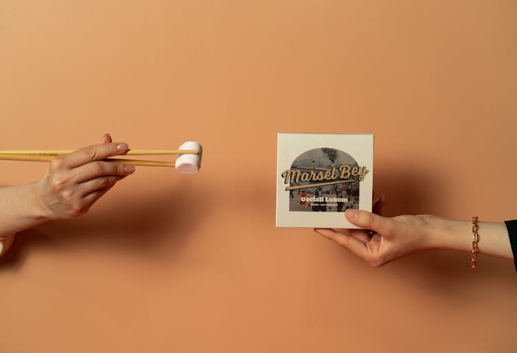 Hands Holding Marshmallow With Chopsticks And Placard