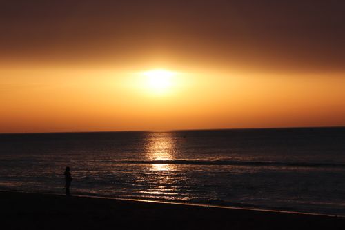 Free A person silhouetted against a tranquil beach sunset, perfect for relaxation themes. Stock Photo