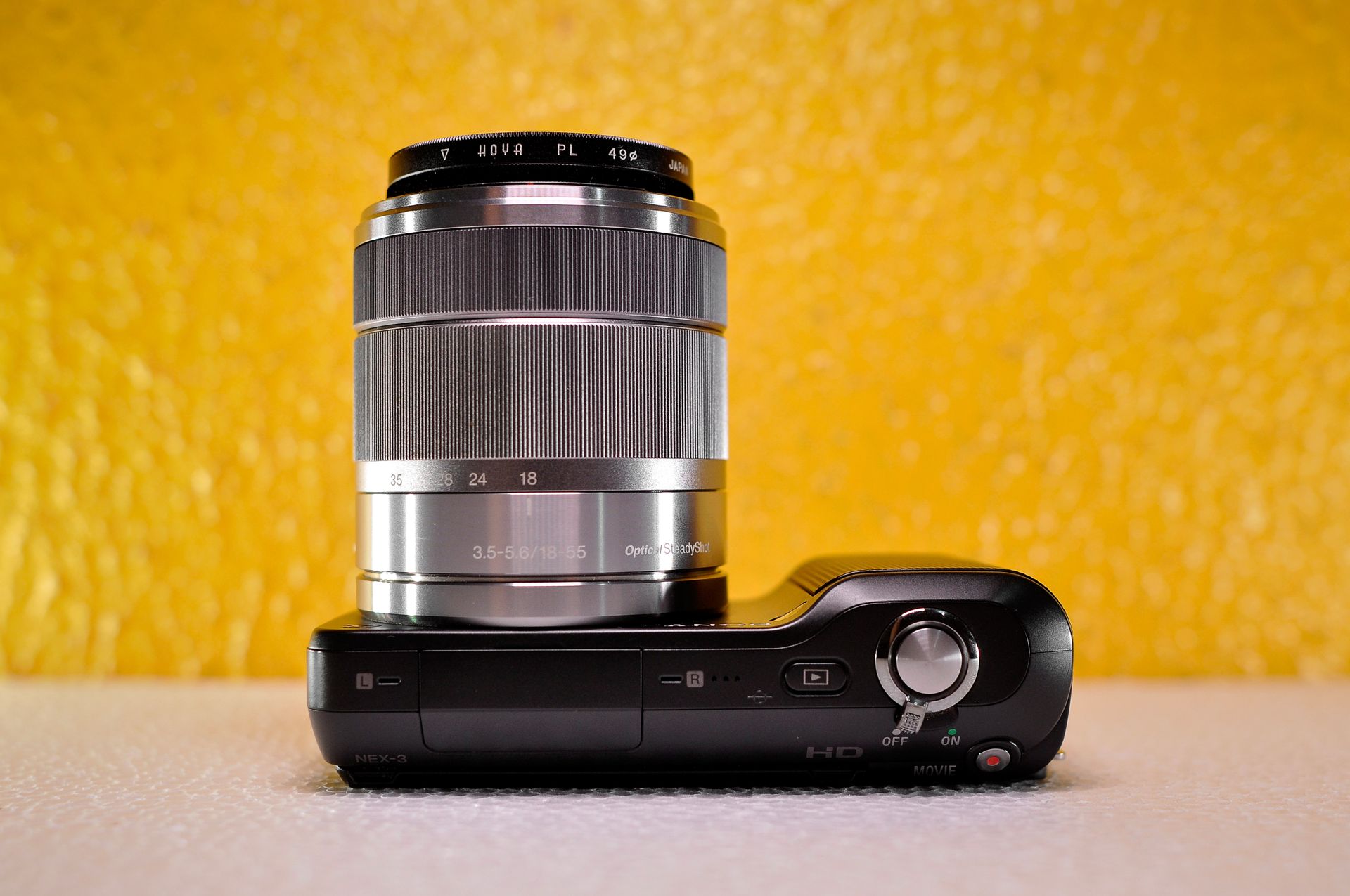 A sleek modern digital camera with a zoom lens against a textured yellow background.