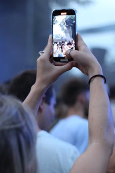 Close-up of a person recording a lively concert scene with a smartphone.