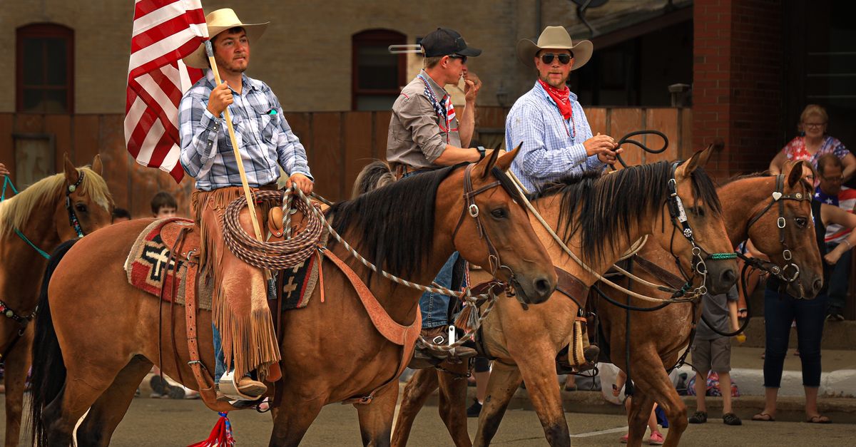 Cowboys parade with horses and American flag on a sunny day outdoors.
