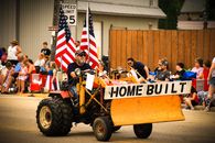 A community parade in Bonduel, WI featuring a man driving a homemade tractor adorned with American flags.