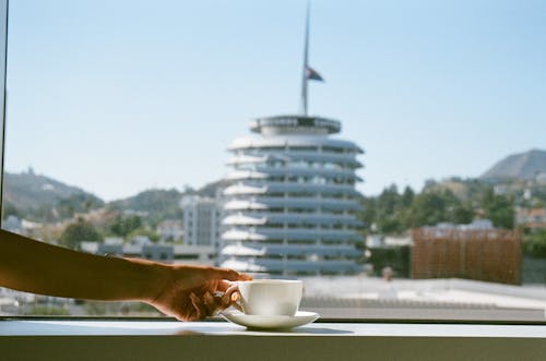Woman Reaching fir a cup of Coffee Standing on a Windowsill with the Capitol Records Building in the Background 