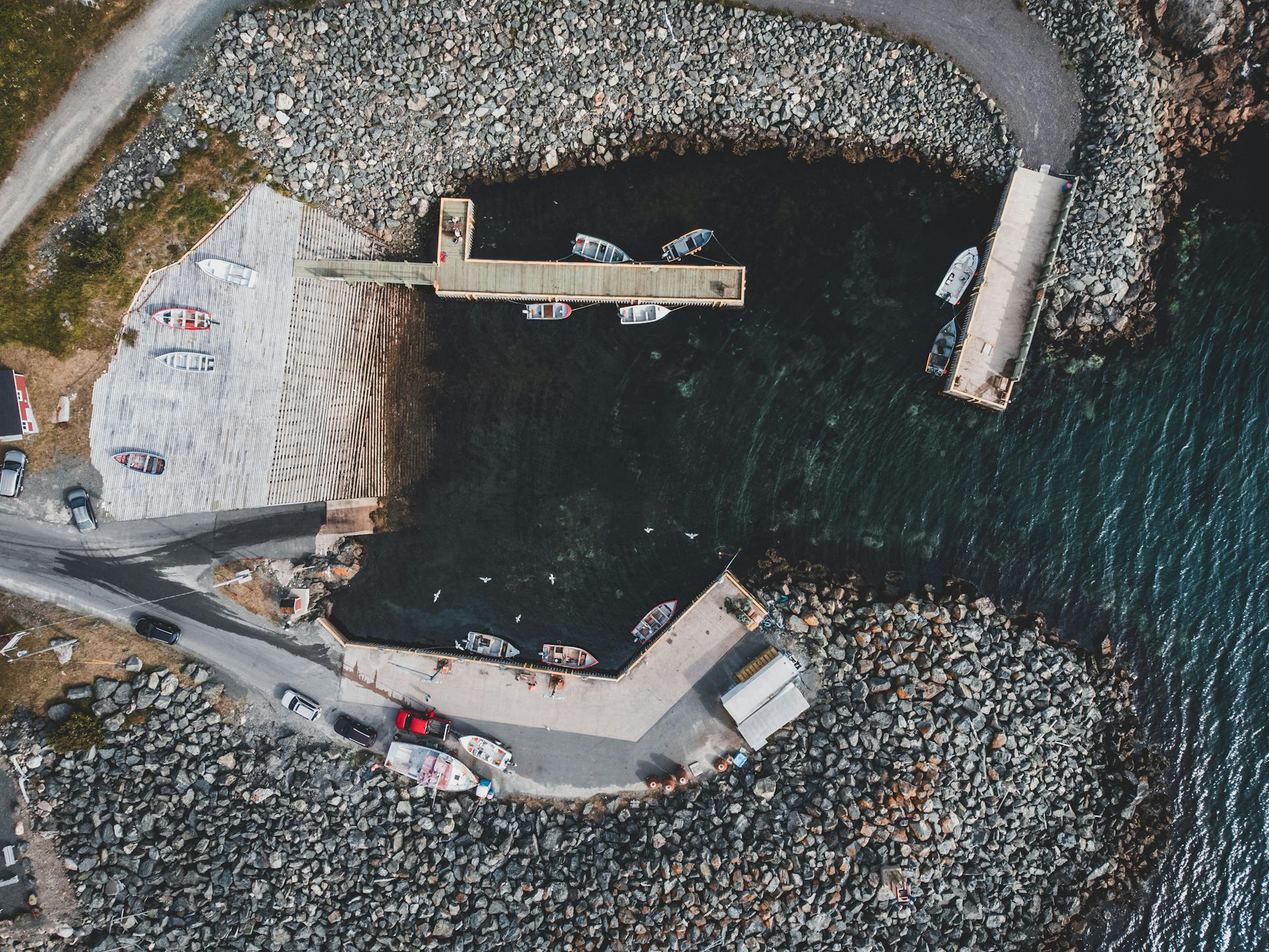 A drone-shot aerial view of a marina with boats docked in a rocky harbor.