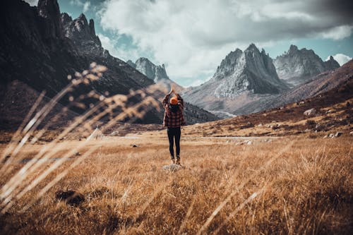 Photo of a Person Raising their Hands while Standing in the Field against the Background of Mountains