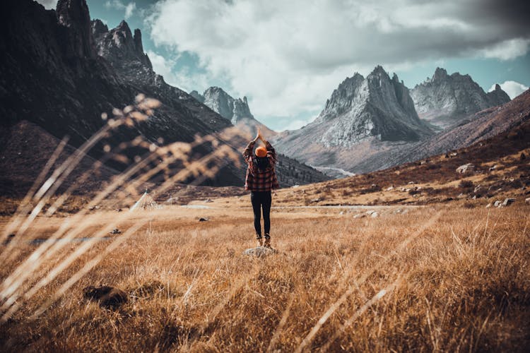 Photo Of A Person Raising Their Hands While Standing In The Field Against The Background Of Mountains