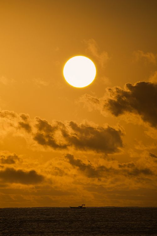 Free Golden sunset over Arraial d'Ajuda's ocean with clouds and distant boat silhouette. Stock Photo