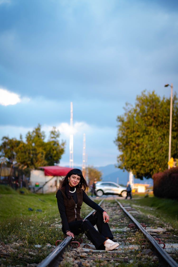 Woman In Black Long Sleeves And Black Pants Sitting On A Railroad Track