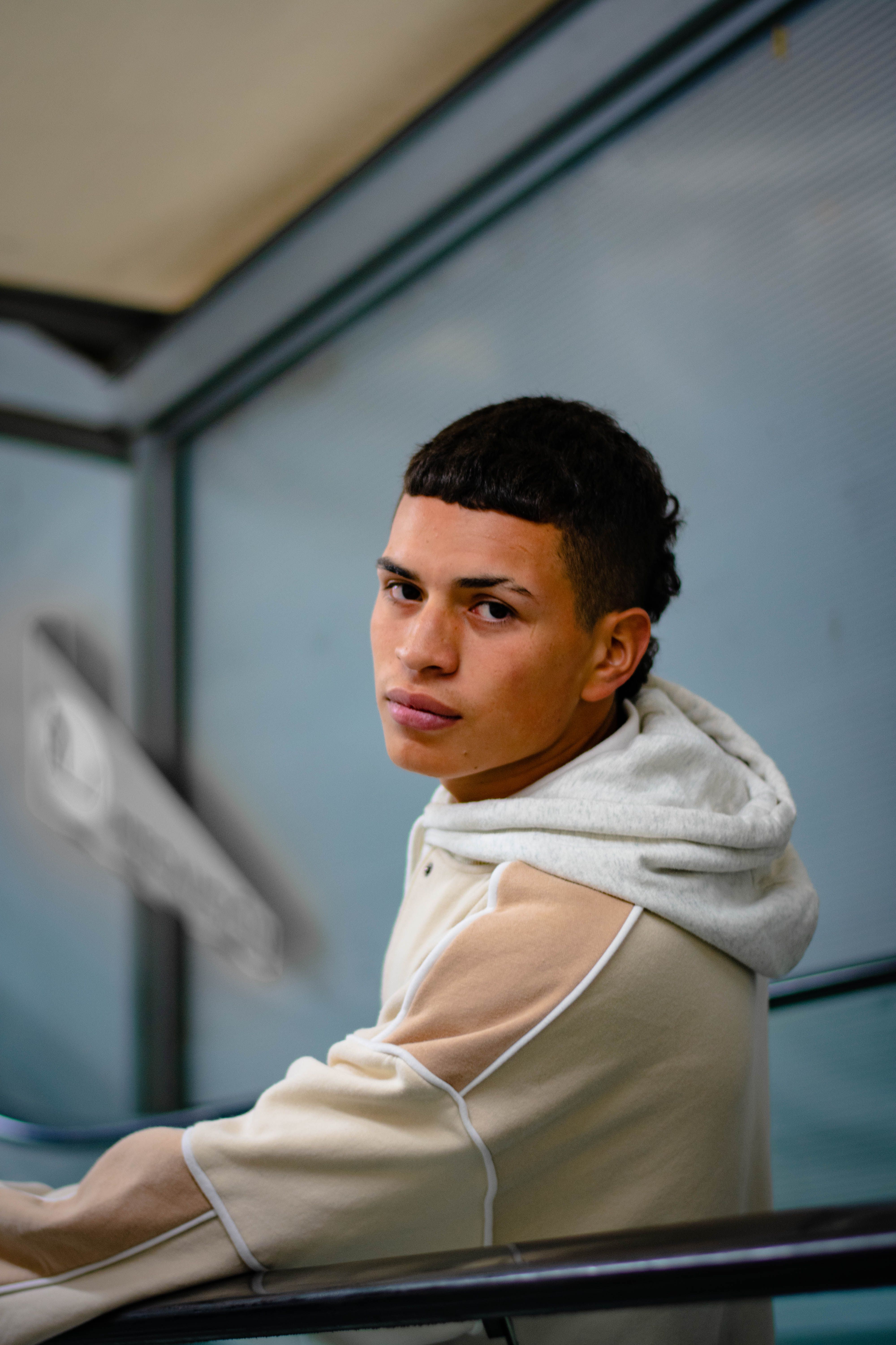 Portrait of a young man in a hoodie, leaning by a rail indoors.