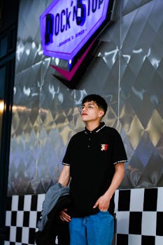 A stylish young man poses under a neon sign in a modern urban environment.